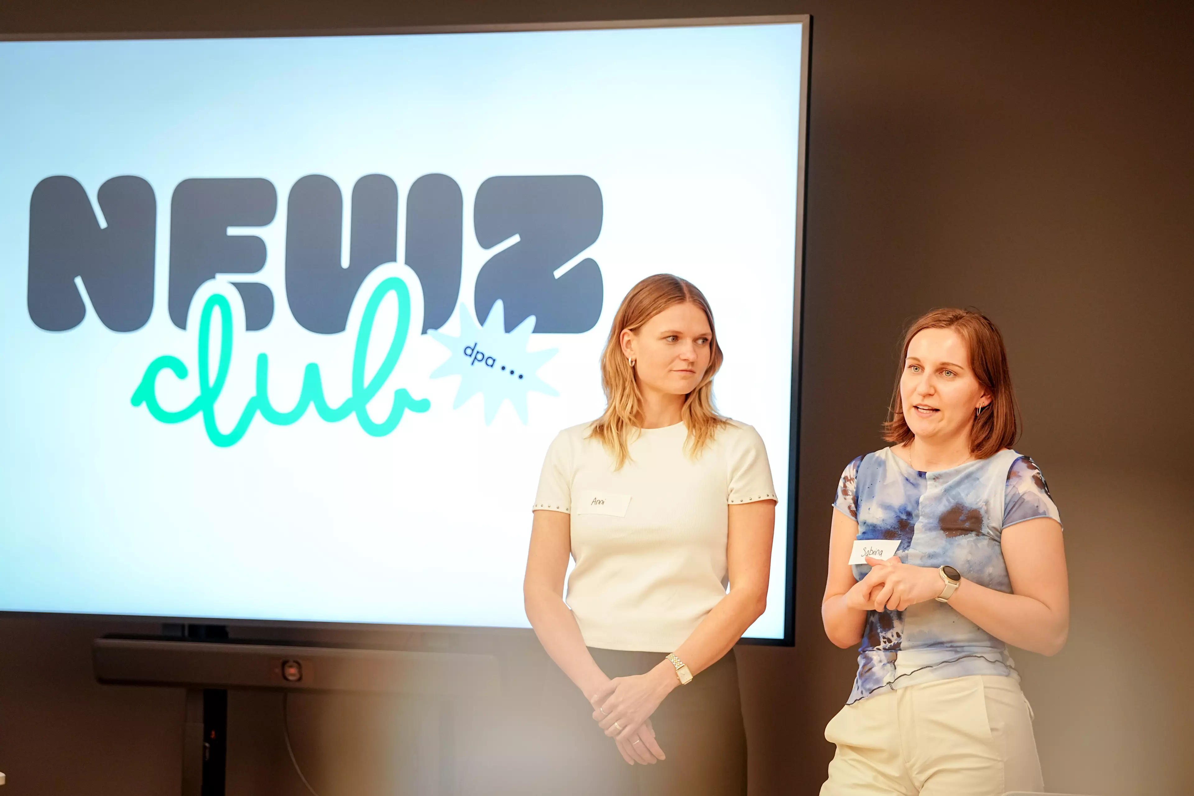 Ann-Marie Utz und Sabrina Szameitat stellen den dpa NewZ Club vor. Sie stehen vor einem großen Bildschirm. Sabrina Szameitat redet.