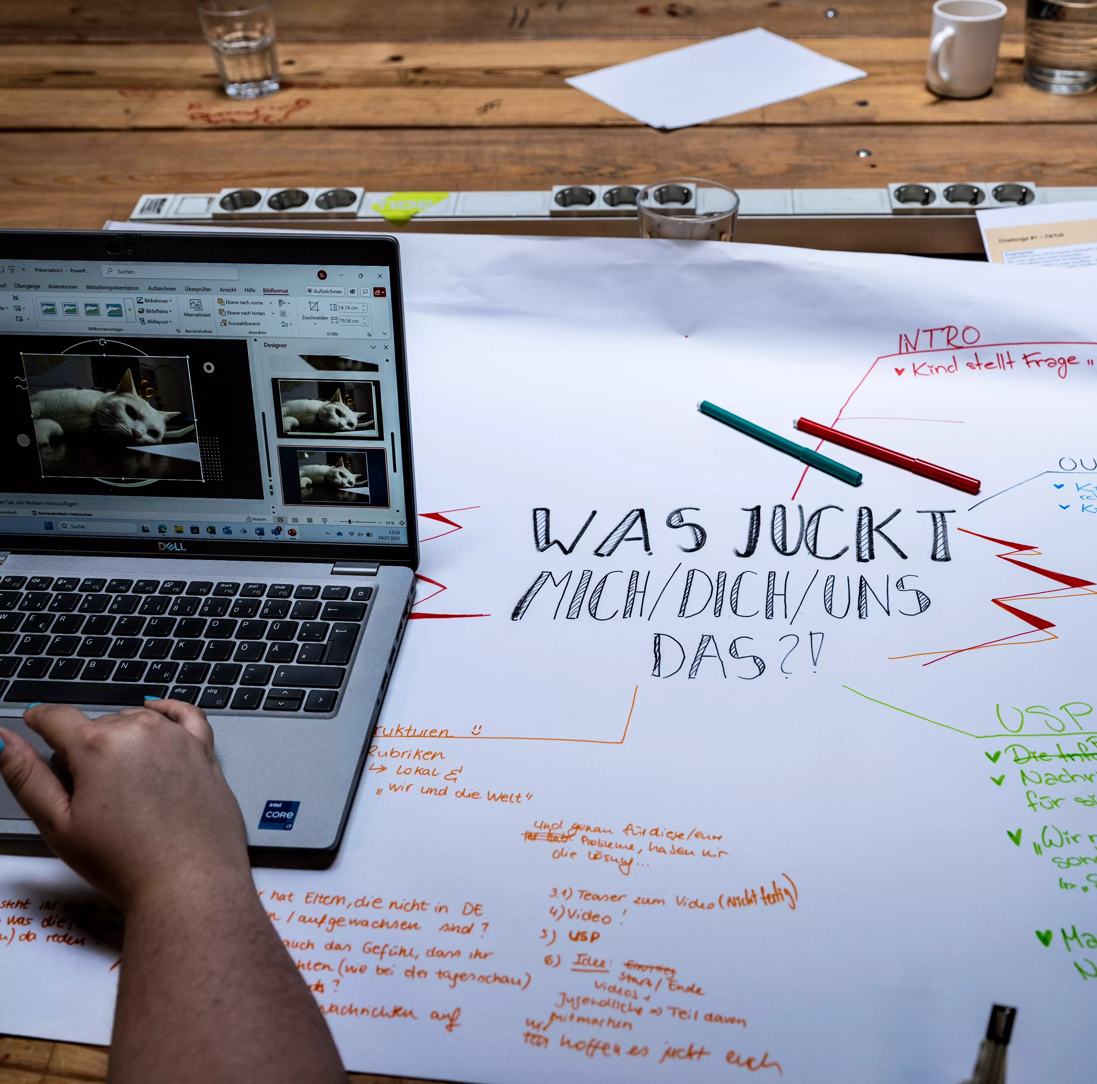 Tisch mit beschriebenem Flipchart-Papier und einem Laptop, der von einer Hand bedient wird (Wolfram Kiwit / Lensing Media)
