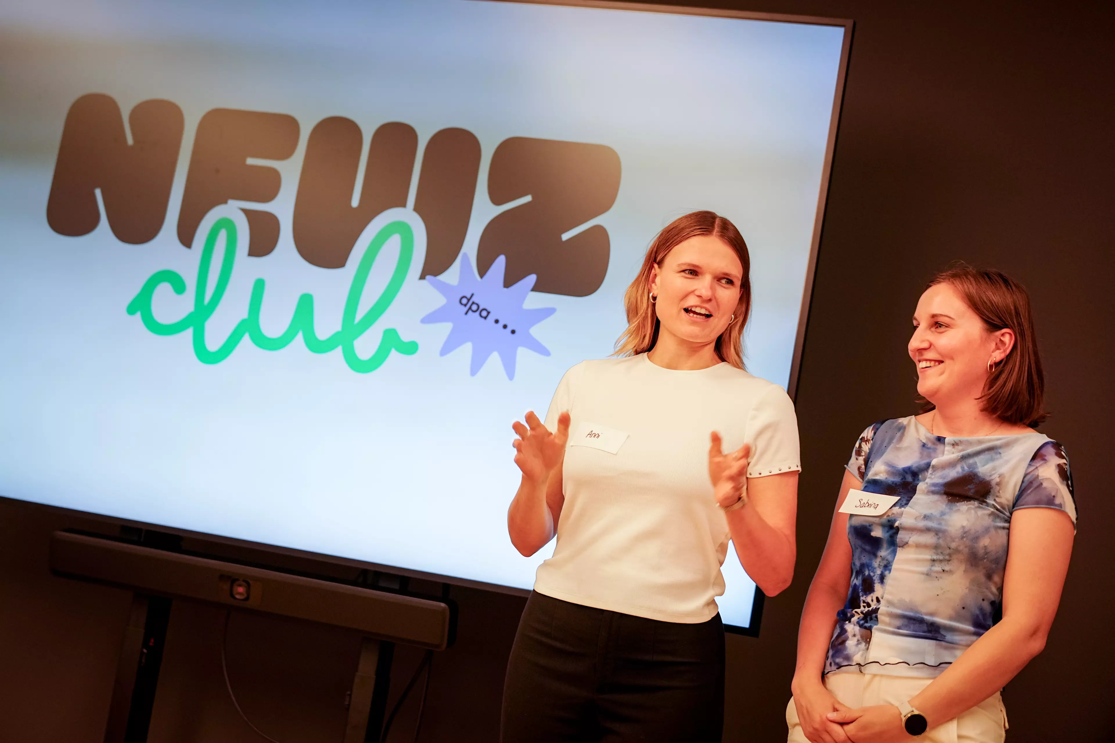 Ann-Marie Utz und Sabrina Szameitat stellen den dpa NewZClub vor. Sie stehen vor einem großen Bildschirm.